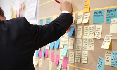 A suited man writes on a board filled with sticky notes, demonstrating the process of using proposal management software.