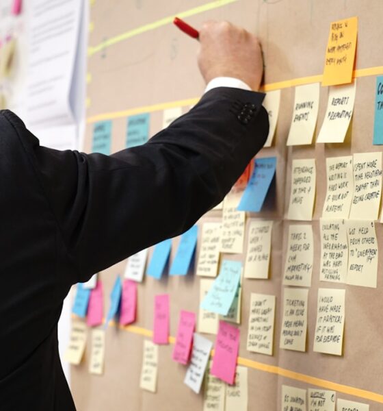 A suited man writes on a board filled with sticky notes, demonstrating the process of using proposal management software.