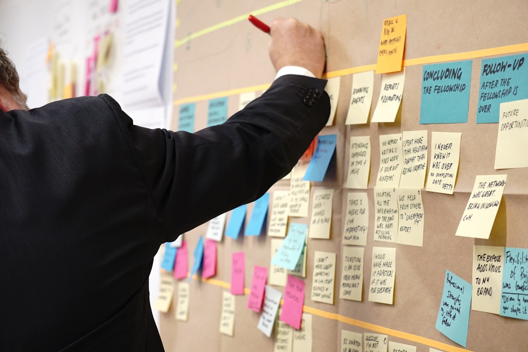A suited man writes on a board filled with sticky notes, demonstrating the process of using proposal management software.